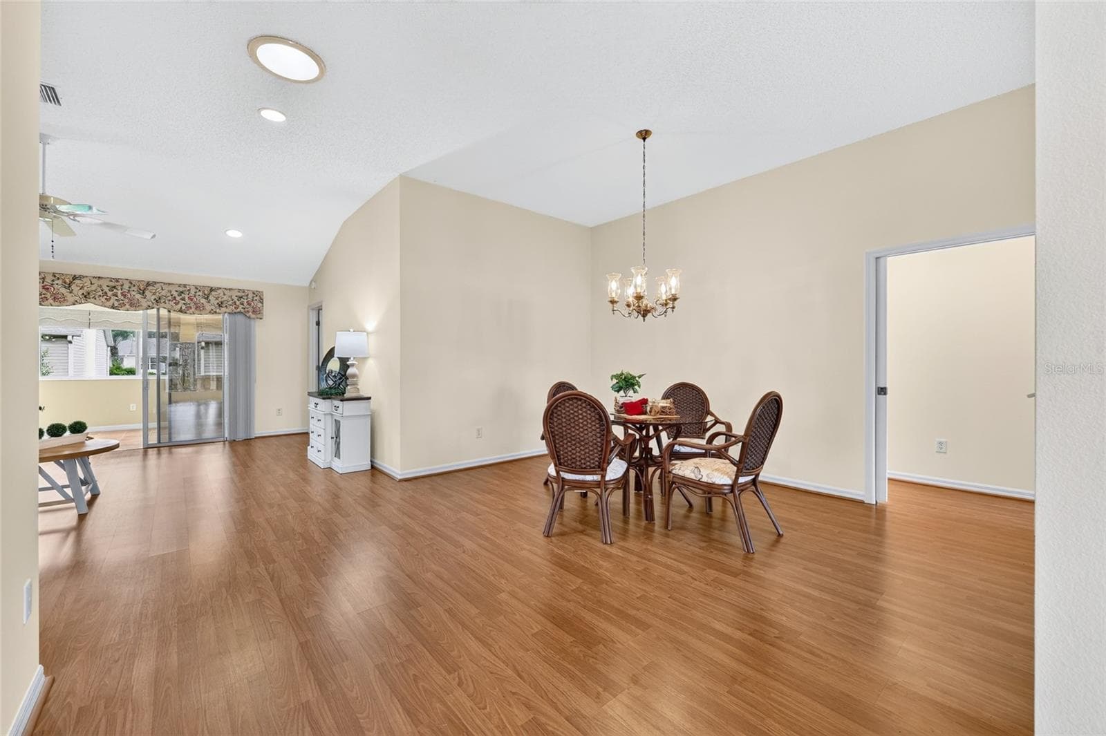 Spacious dining area featuring wood-look flooring, vaulted ceilings, a decorative chandelier, and an open layout that flows into the living space. - 3064 BURBANK LN, THE VILLAGES