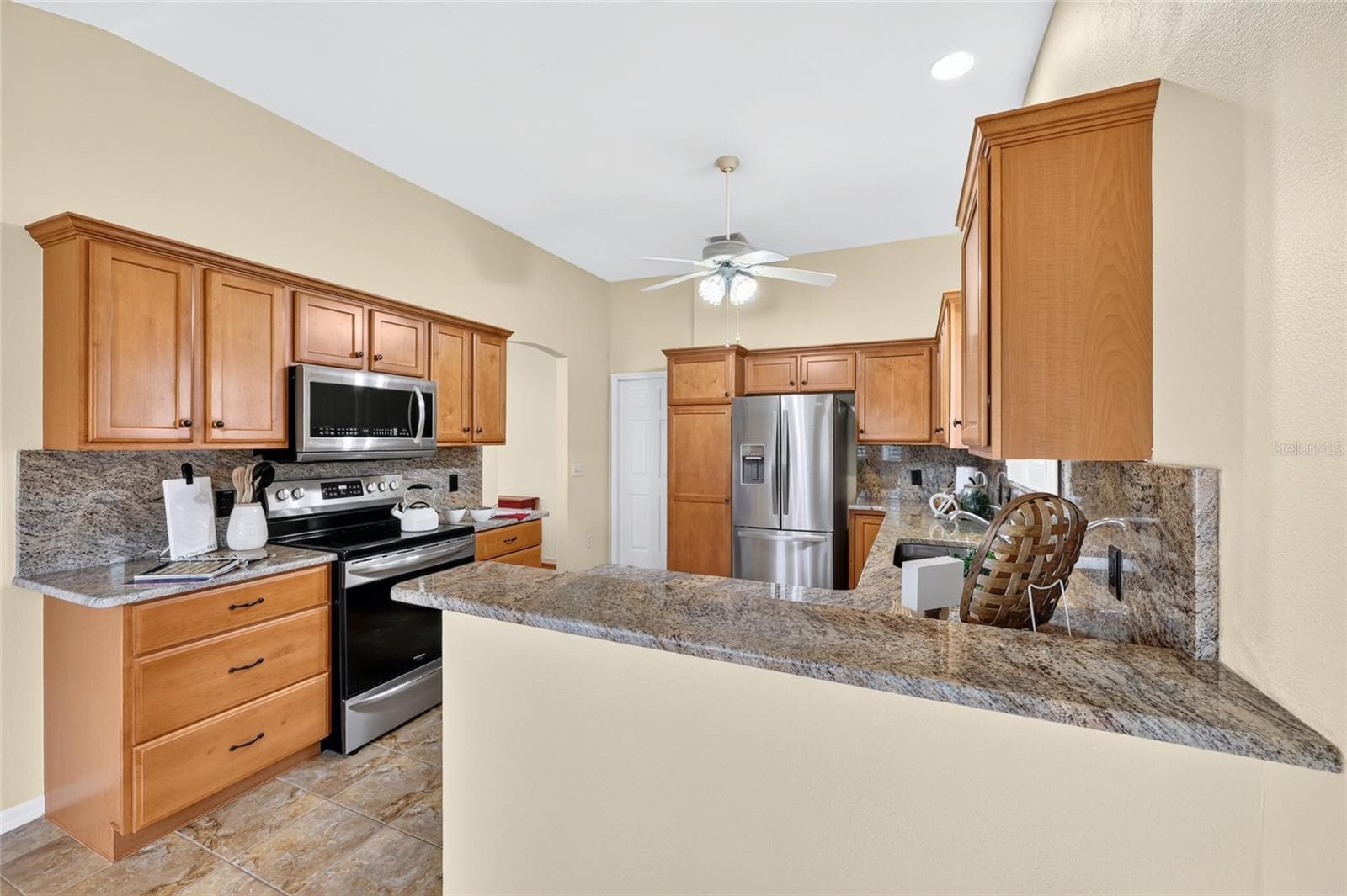Well-appointed kitchen featuring granite countertops and backsplash, warm wood cabinetry, stainless steel appliances, and a convenient breakfast bar. - 3064 BURBANK LN, THE VILLAGES