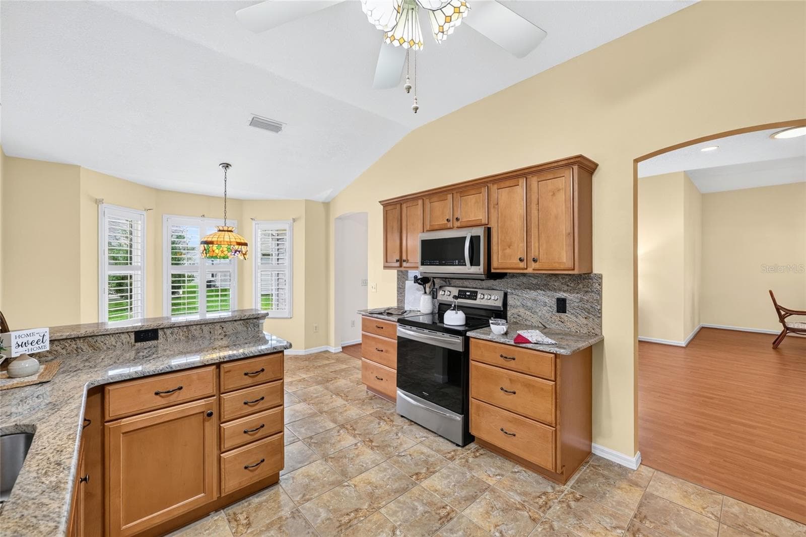 Spacious kitchen featuring vaulted ceilings, generous cabinetry, granite countertops, tile flooring, and an adjoining breakfast nook filled with natural light. - 3064 BURBANK LN, THE VILLAGES