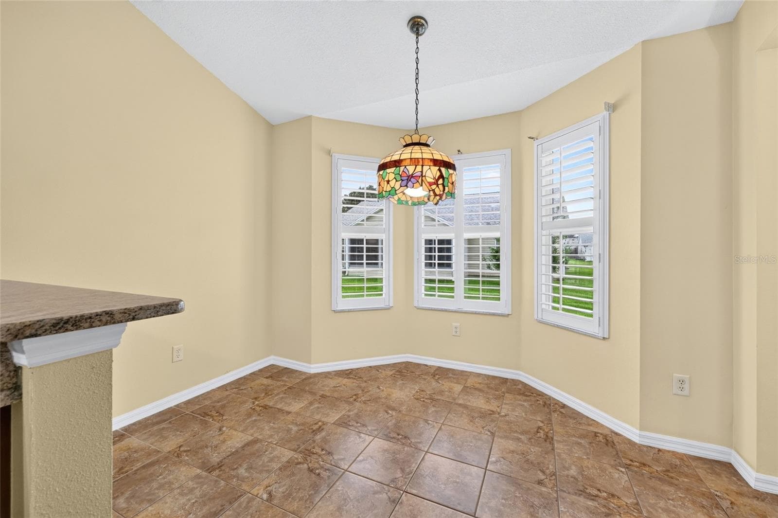 Charming breakfast nook featuring a bay-style window arrangement with plantation shutters, decorative pendant lighting, and easy access to the kitchen. - 3064 BURBANK LN, THE VILLAGES