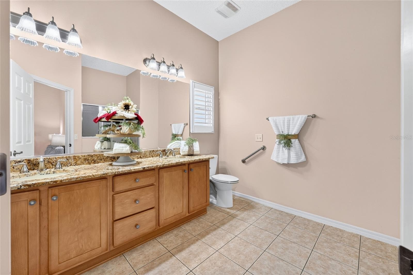 Primary bathroom featuring a double-sink vanity with granite countertops, generous cabinet storage, tile flooring, and a large vanity mirror. - 3064 BURBANK LN, THE VILLAGES