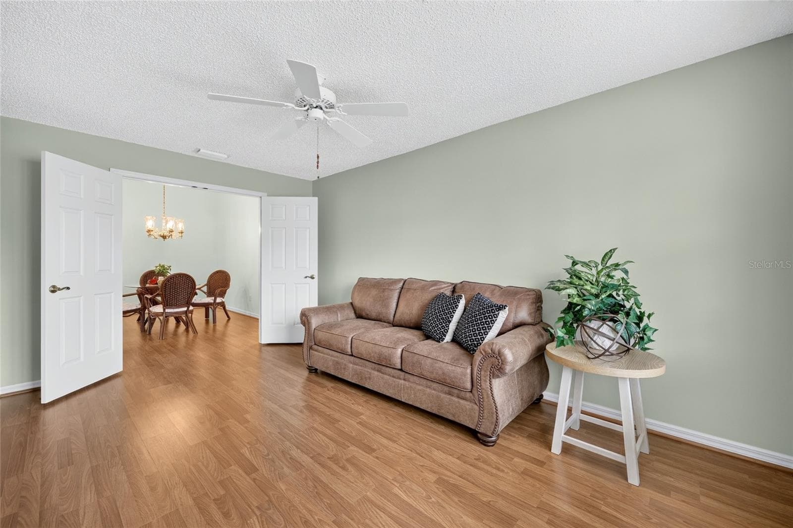 Versatile room featuring wood-look flooring, a ceiling fan, soft neutral wall colors, and double doors opening to the dining area. Ideal for a home office, den, bedroom, or additional living space. - 3064 BURBANK LN, THE VILLAGES