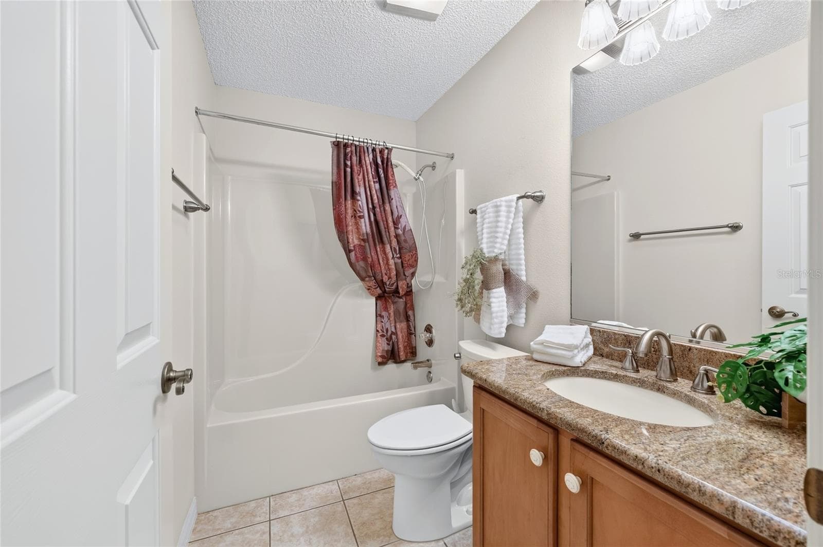 Guest bathroom featuring a granite-topped vanity, wood cabinetry, tile flooring, and a combination bathtub and shower. - 3064 BURBANK LN, THE VILLAGES