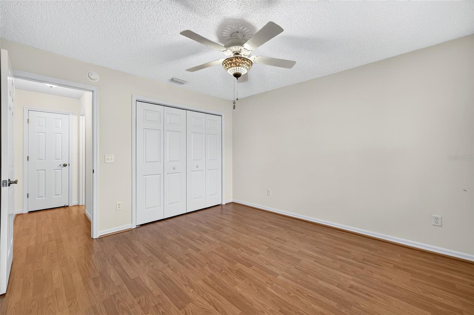 Comfortable guest bedroom featuring wood-look flooring, a decorative ceiling fan, neutral walls, and a spacious double-door closet. - 3064 BURBANK LN, THE VILLAGES