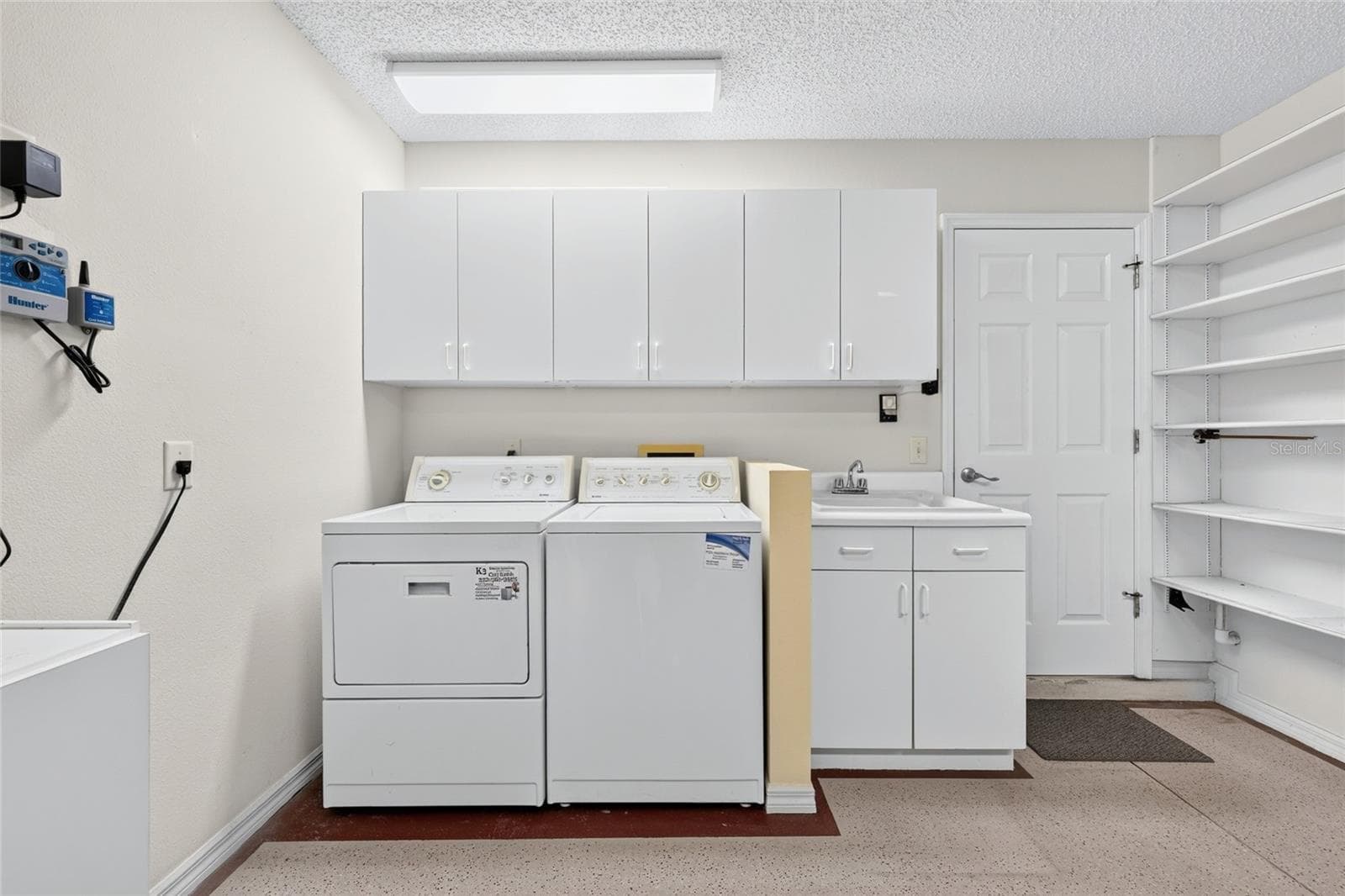 Convenient laundry area featuring a washer and dryer, utility sink, overhead cabinetry, and open shelving for additional storage and organization. - 3064 BURBANK LN, THE VILLAGES