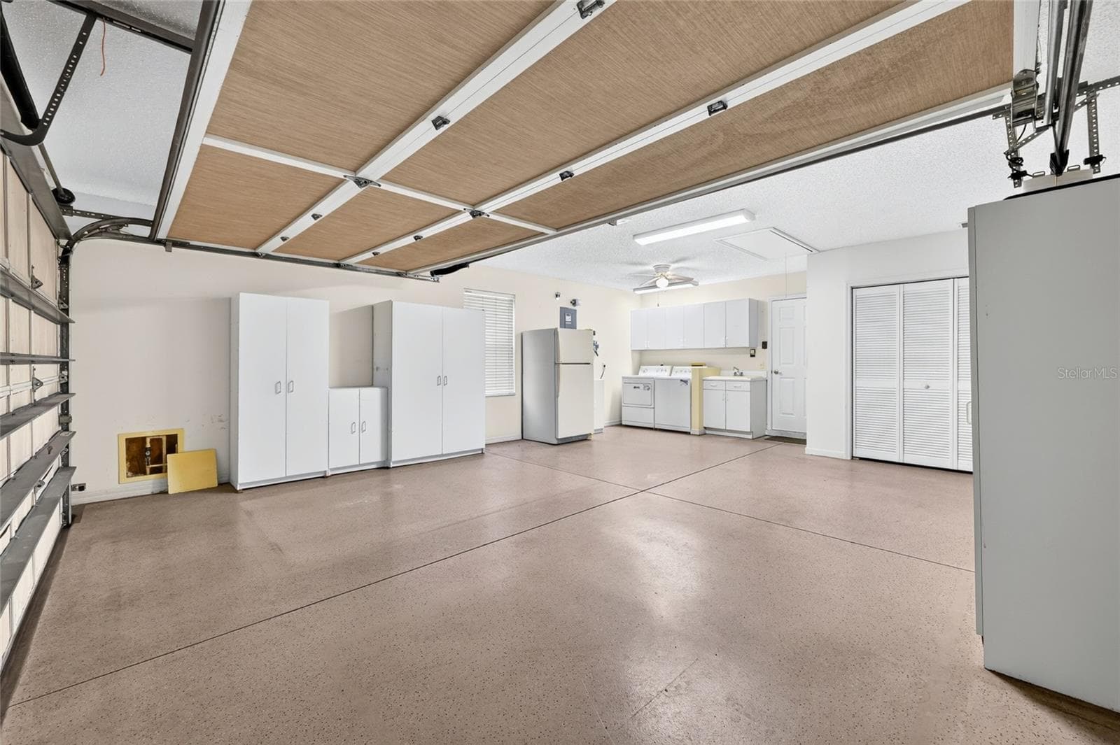 Spacious two-car garage offering extensive storage cabinetry, a utility sink, laundry area, refrigerator, and room for vehicles and additional storage. - 3064 BURBANK LN, THE VILLAGES