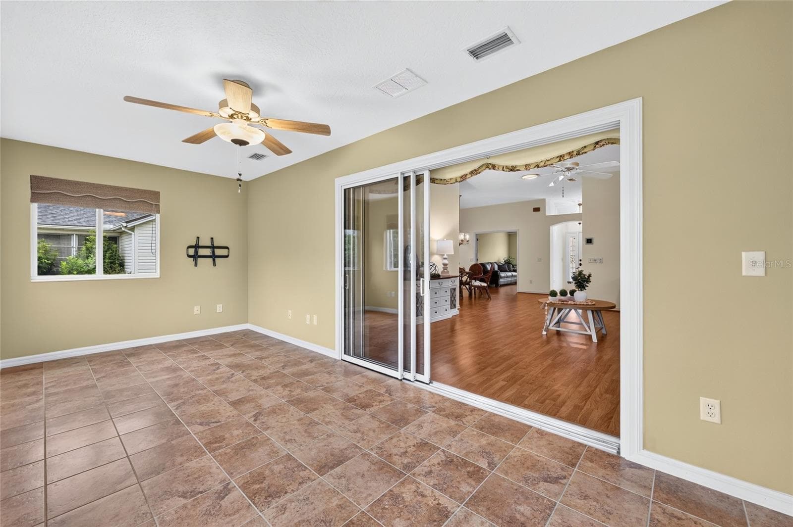 Light-filled enclosed lanai featuring tile flooring, a ceiling fan, and sliding glass doors connecting to the main living area. A versatile space for relaxing or entertaining. - 3064 BURBANK LN, THE VILLAGES
