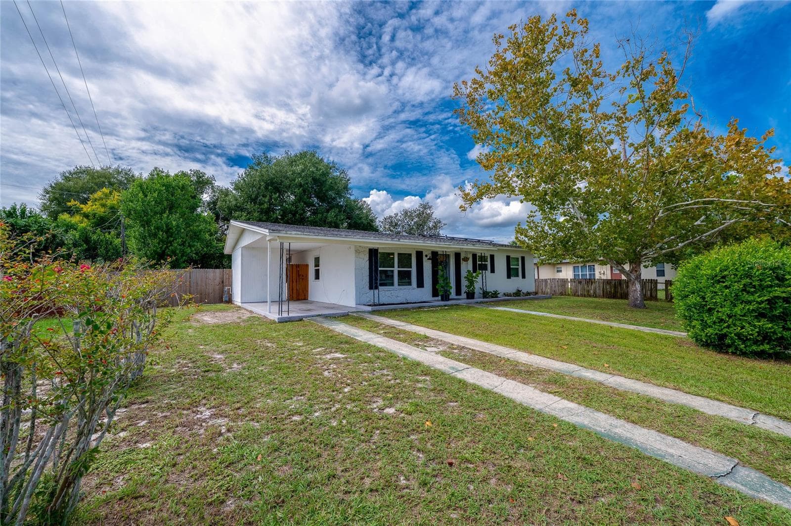 Exterior view highlighting the long concrete ribbon driveway, expansive front lawn, mature shade trees, and low-maintenance single-story design. - 605 E NORMANDY BLVD, DELTONA