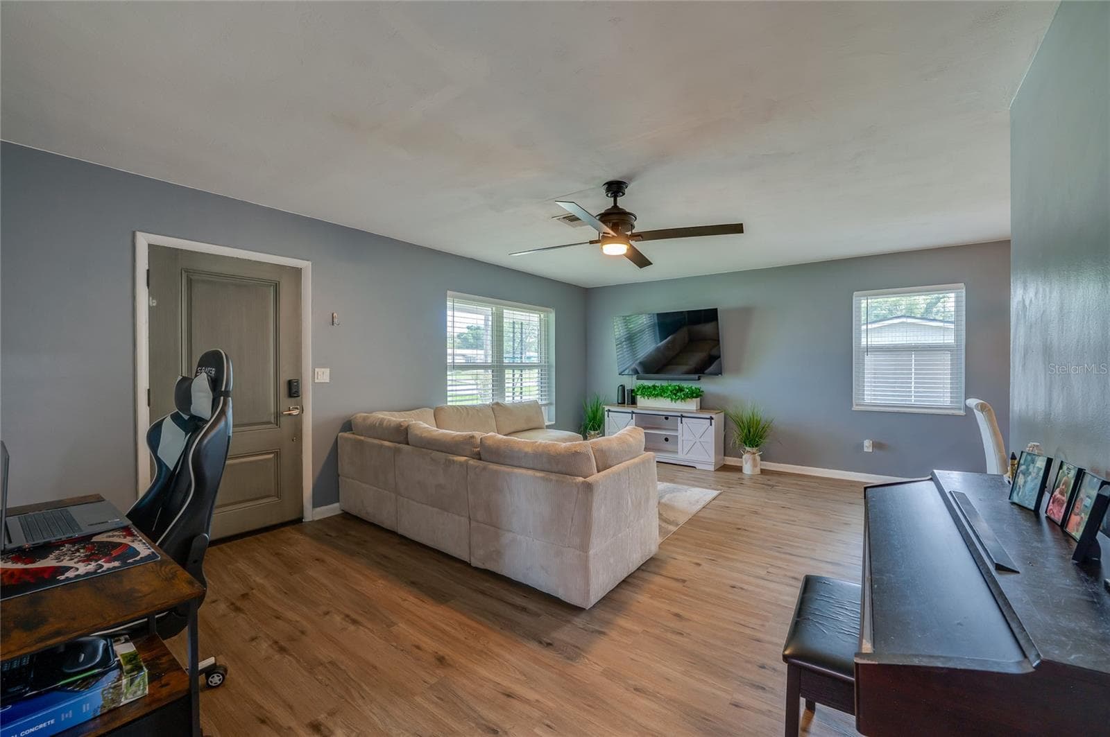 Open living area showing LVP floors, cool gray walls, a ceiling fan, and large windows that fill the space with light. - 605 E NORMANDY BLVD, DELTONA