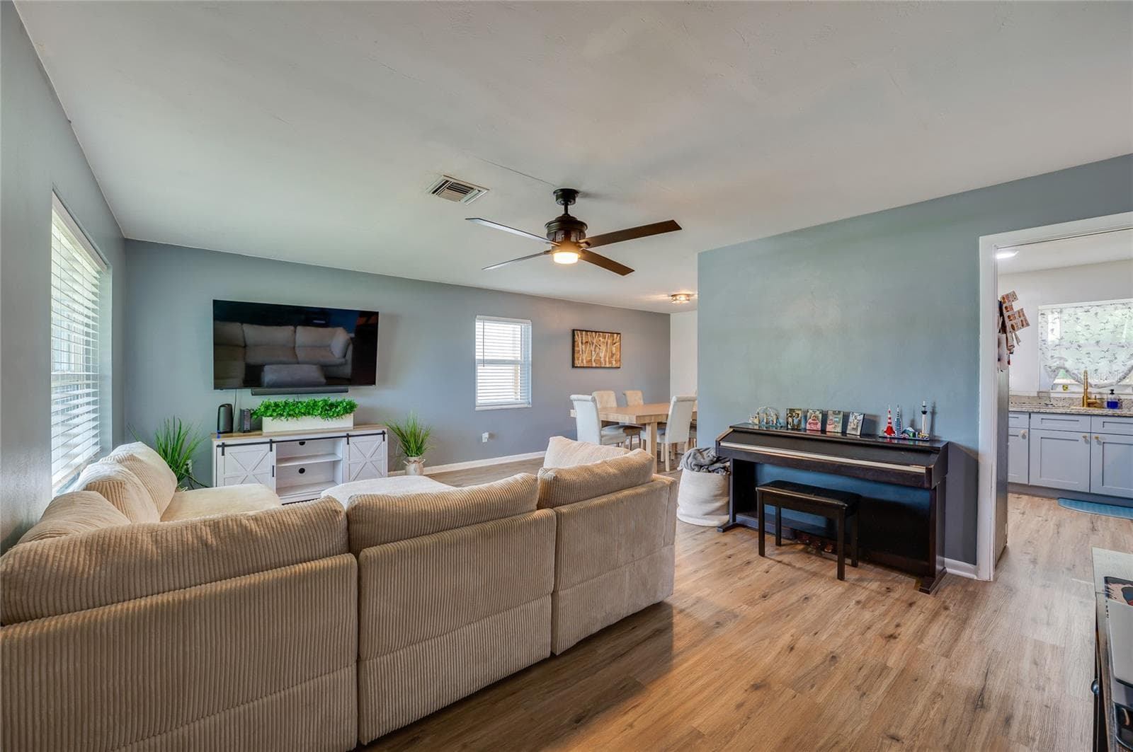 Expansive open-concept living space with LVP flooring, ceiling fans, and seamless flow into adjoining dining and kitchen areas. - 605 E NORMANDY BLVD, DELTONA