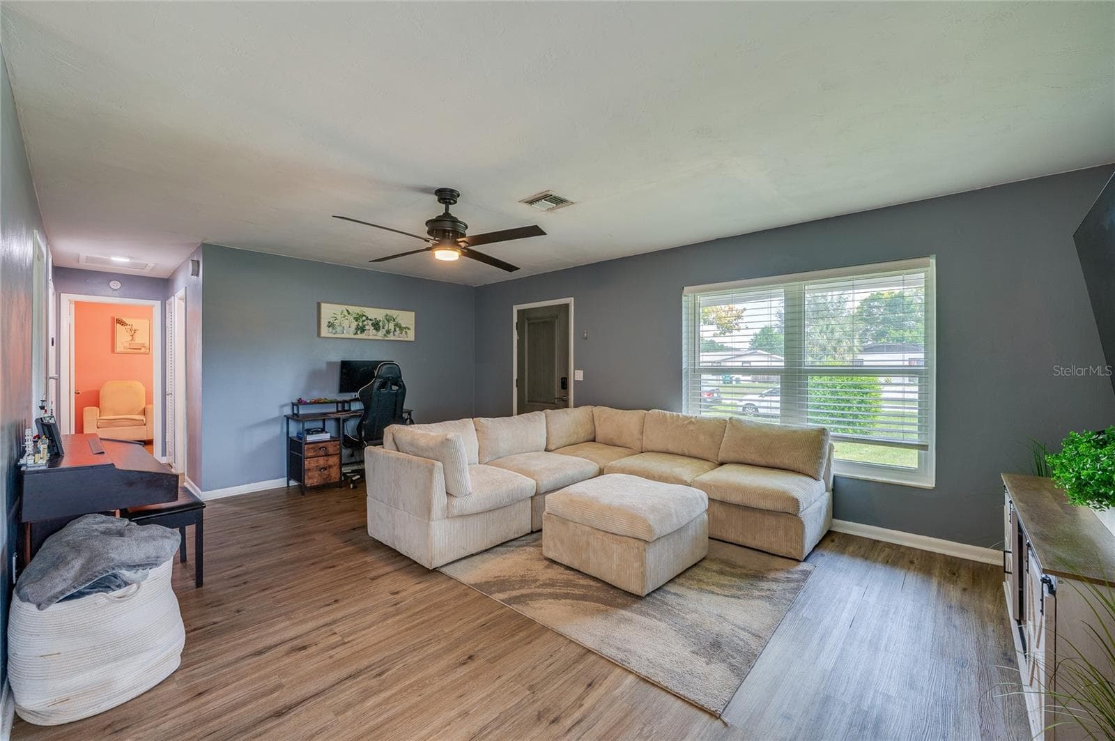 Generously sized main room featuring LVP flooring, soft gray walls, a central ceiling fan, and large front-facing windows. - 605 E NORMANDY BLVD, DELTONA