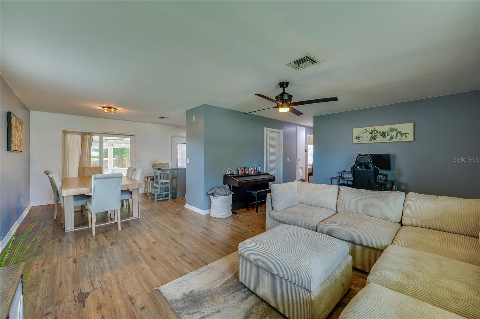 Broad view of an open layout emphasizing natural LVP floors, a ceiling fan, and clear sightlines between living and dining spaces. - 605 E NORMANDY BLVD, DELTONA