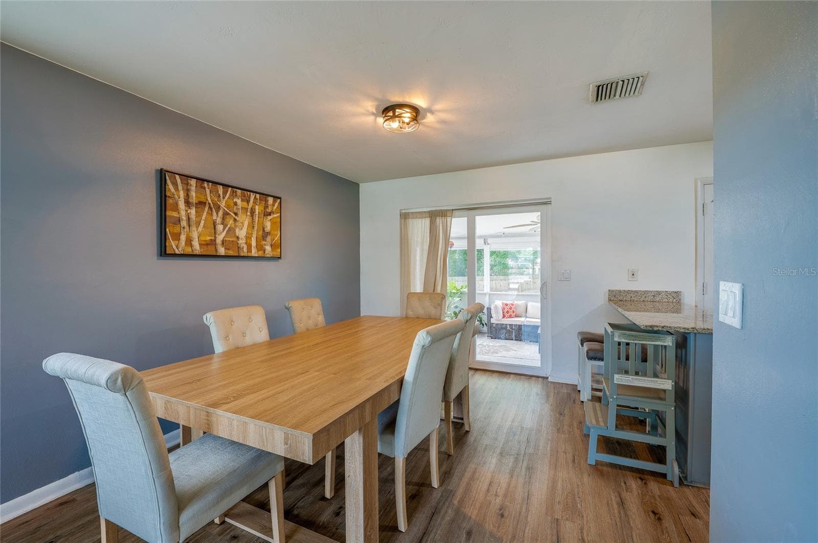 Light-filled dining area featuring LVP flooring, accent wall paint, and sliding glass doors that lead directly out to a covered patio space. - 605 E NORMANDY BLVD, DELTONA
