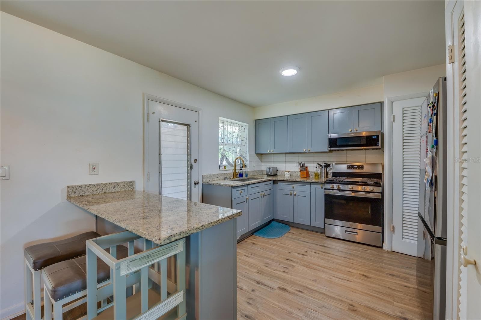 Functional kitchen layout displaying blue cabinetry, granite counter space, stainless steel appliances, and built-in breakfast bar overhangs. - 605 E NORMANDY BLVD, DELTONA