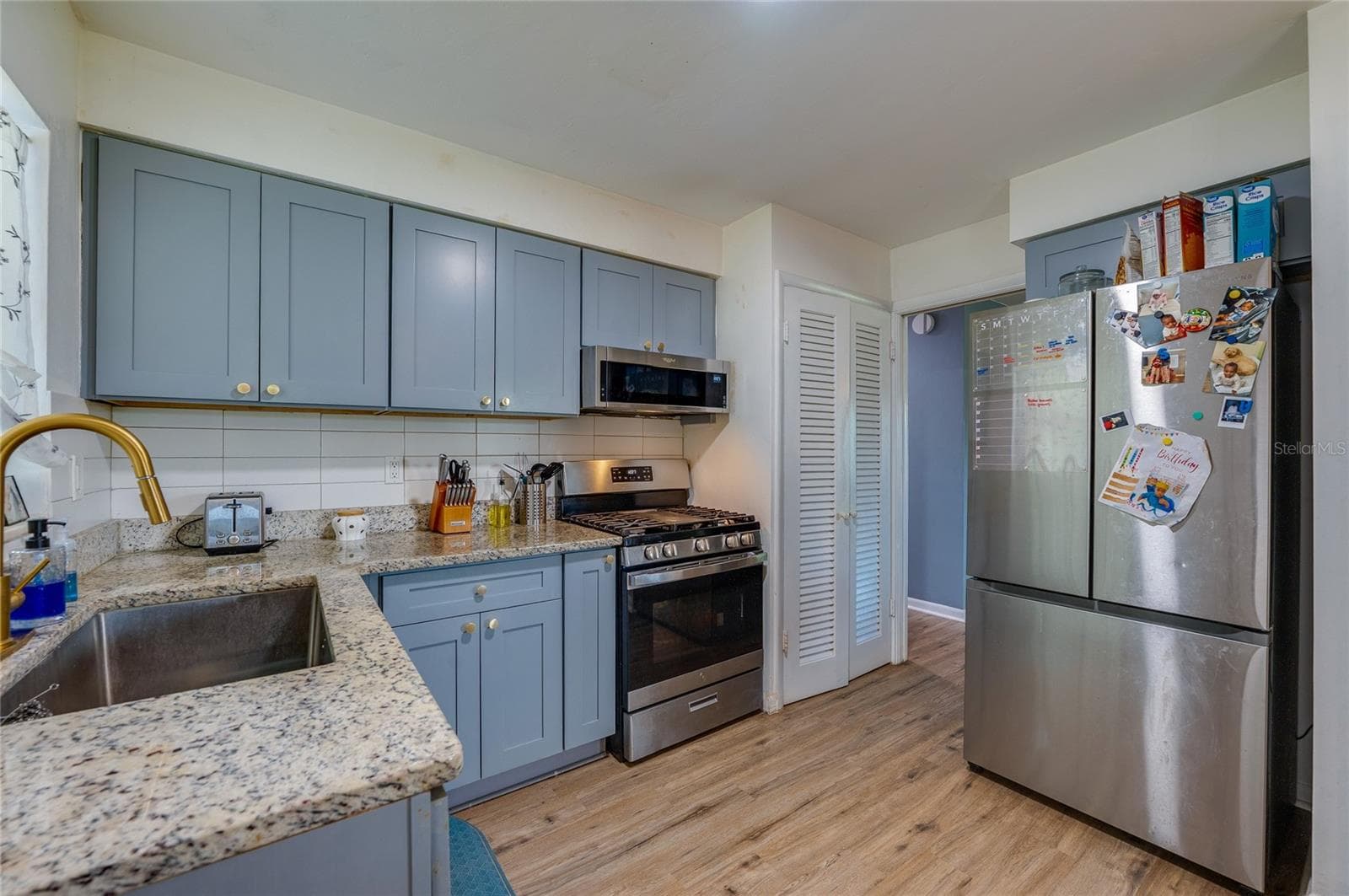 Modernized kitchen with stylish gray-blue cabinets, granite countertops, tile backsplash, and a large stainless steel refrigerator. - 605 E NORMANDY BLVD, DELTONA