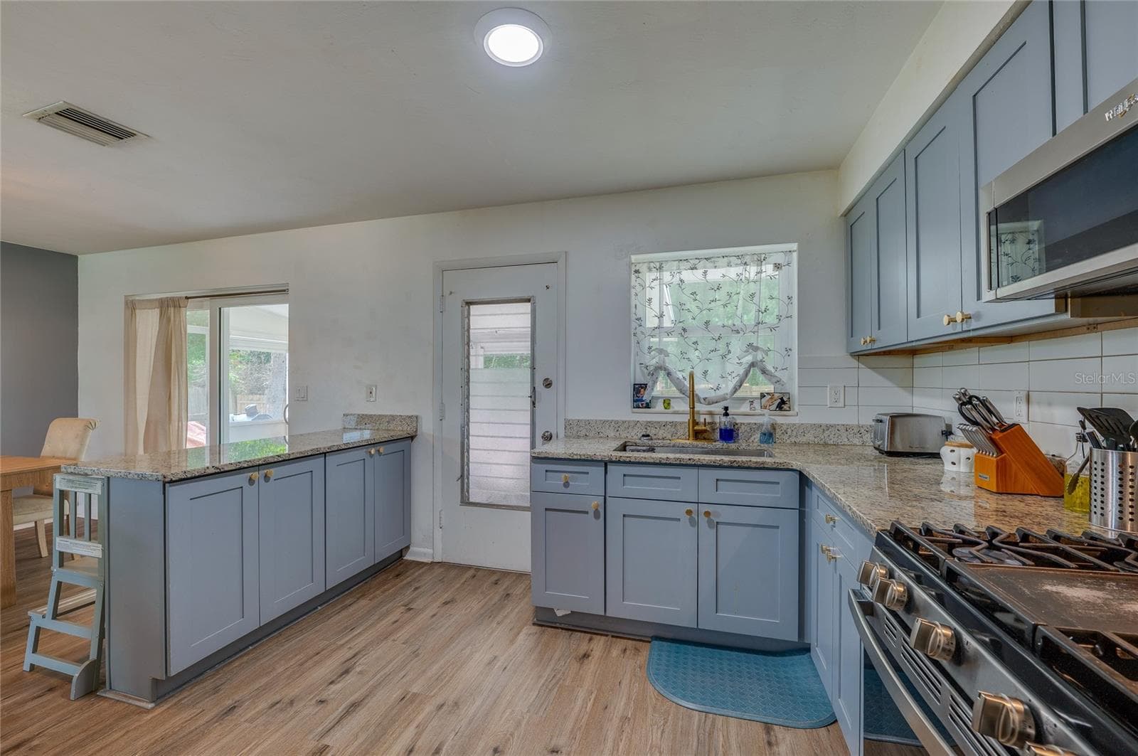 Well-appointed kitchen setup complete with an electric range stove, stainless steel appliances, granite counters, and direct outdoor access. - 605 E NORMANDY BLVD, DELTONA