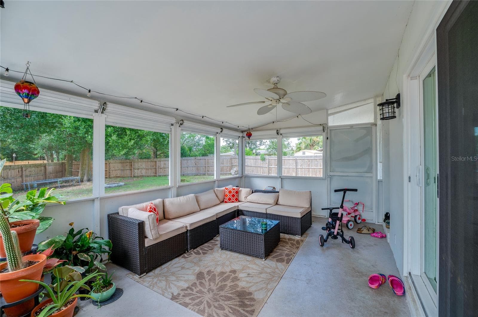 Enclosed, screened-in porch with ceiling fans and surrounding mesh screens overlooking the fenced backyard area. - 605 E NORMANDY BLVD, DELTONA