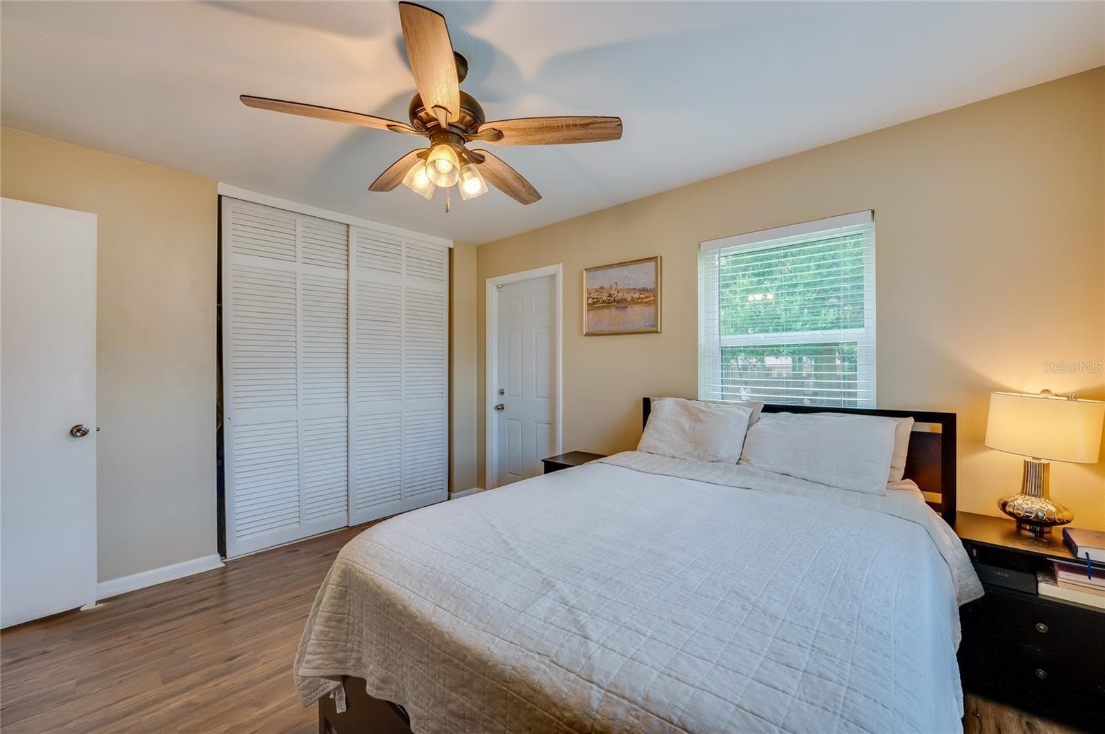 Spacious bedroom featuring warm LVP flooring, white louvered sliding closet doors, and multiple windows allowing plenty of natural light. - 605 E NORMANDY BLVD, DELTONA