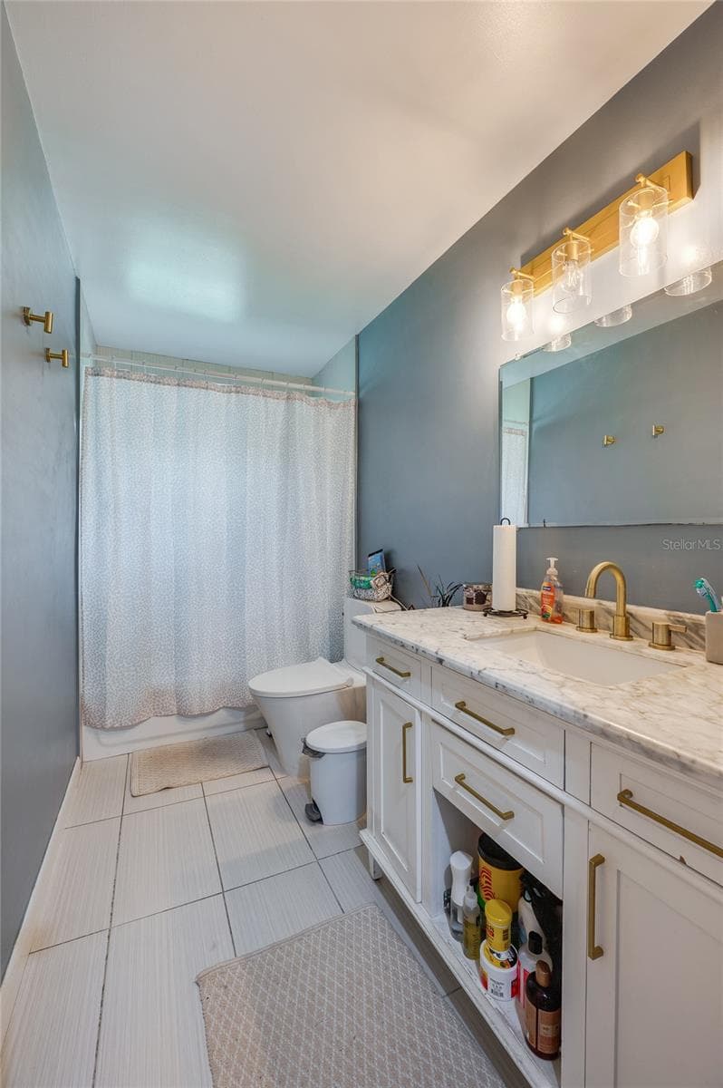 Bathroom displaying a single vanity with gold hardware, modern lighting fixtures, neutral tile flooring, and clean wall finishes. - 605 E NORMANDY BLVD, DELTONA