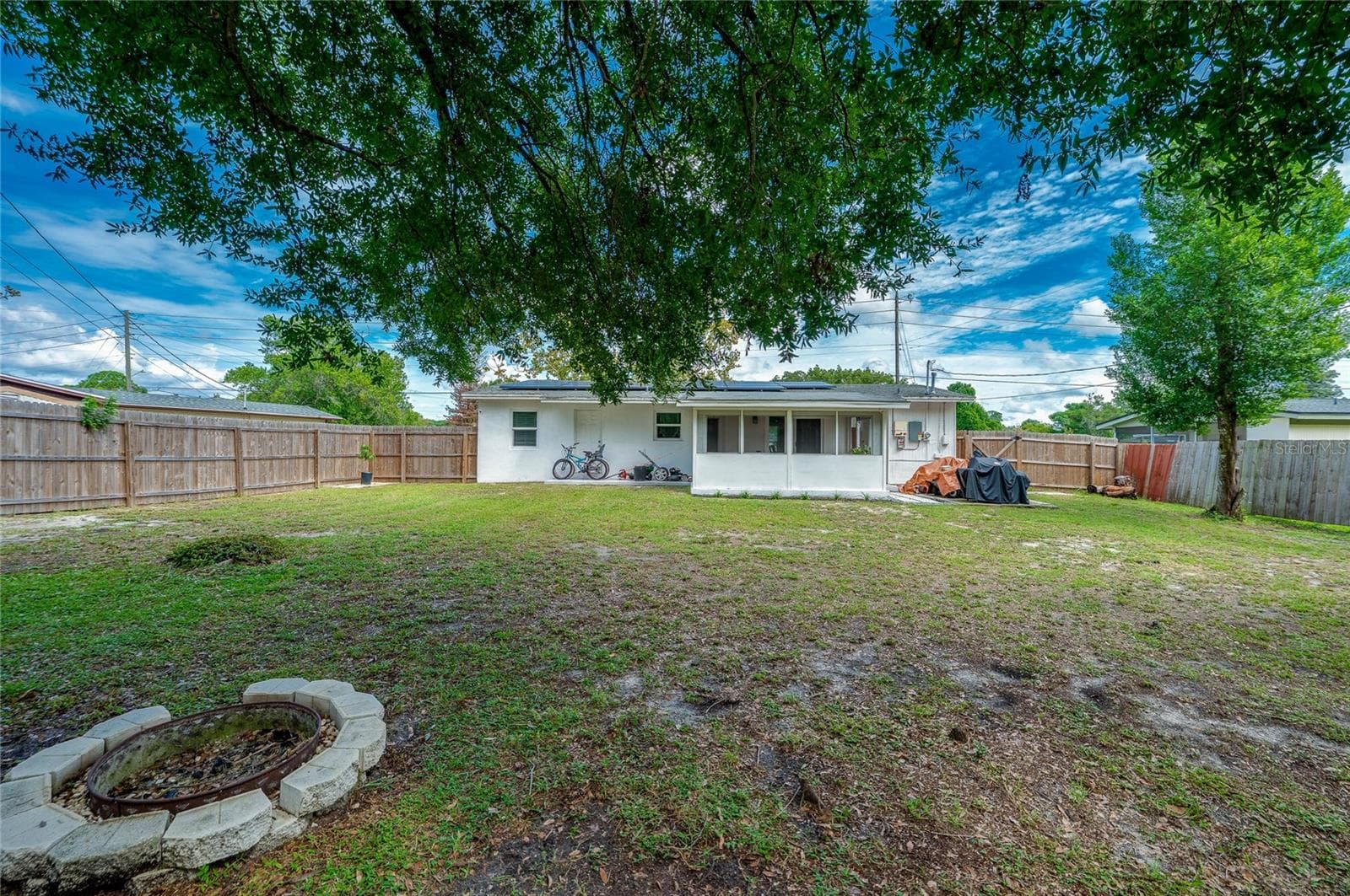 Generous rear lawn featuring a stone fire pit ring, full wood fencing, and direct views of the home's screened patio extension. - 605 E NORMANDY BLVD, DELTONA