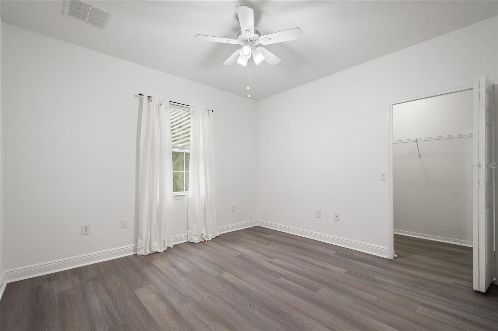 Bedroom 2 with a walk in closet, ceiling fan, drapery rod (drapes do not convey) as well as it is finished in the same luxury plank vinyl. - 1300 EASTERN PECAN PL #208, WINTER GARDEN
