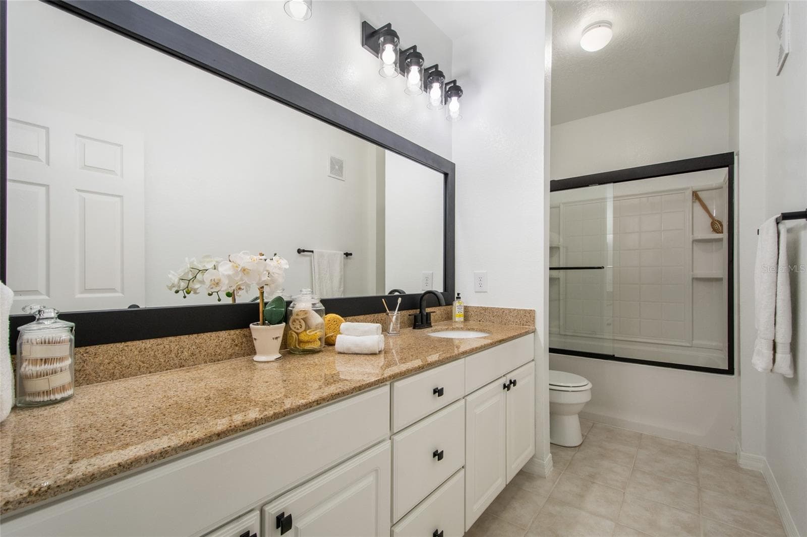 The supporting bathroom between bedrooms 2 and 3 features a elongated vanity with plenty of storage, new MOEN faucet and tub/shower plumbing fixtures, granite countertop, newly framed and painted mirror and brand new light fixtures, toilet paper holder and a convenient towel bar complete this spacious bathroom. Note also the framed glass shower door and built in shower shelving for all your bathroom supplies. - 1300 EASTERN PECAN PL #208, WINTER GARDEN