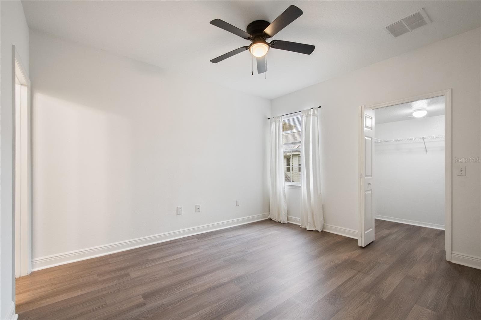 An alternate view of the primary suite looking towards the walk in closet and window which has a lovely view of the surrounding area and allows natural light to flood the room. - 1300 EASTERN PECAN PL #208, WINTER GARDEN