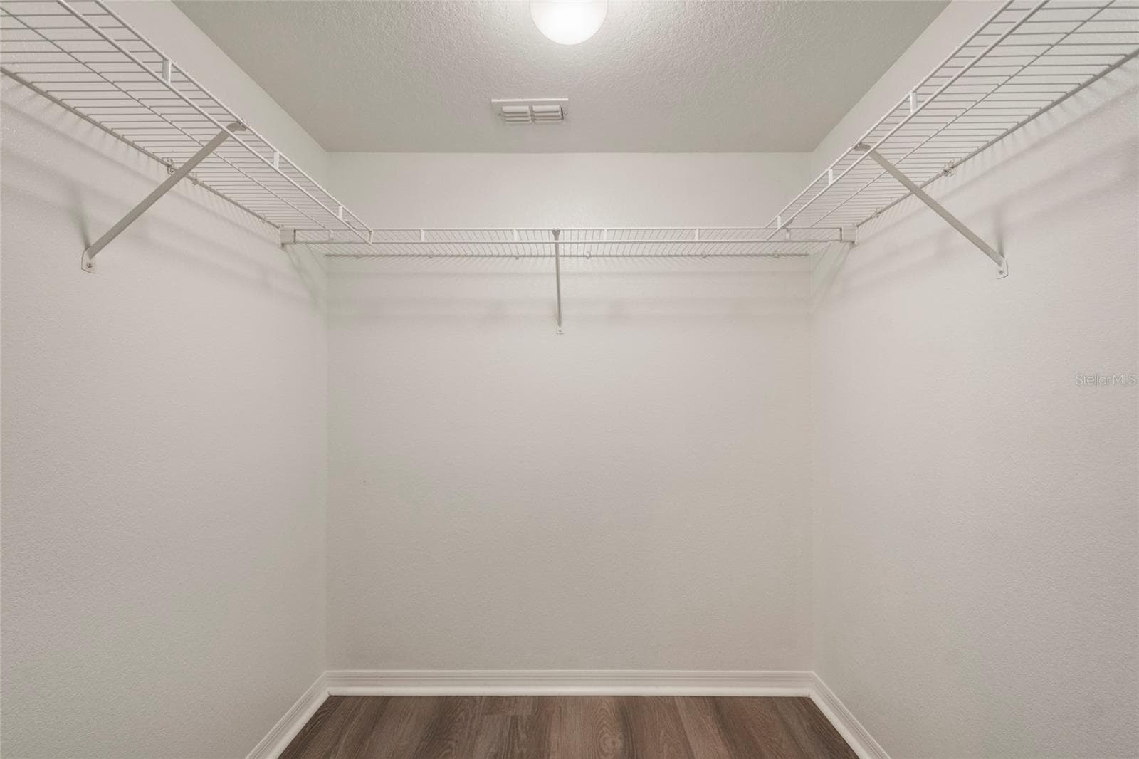Primary suite closet equipped with light, shelving and finished with luxury plank vinyl flooring. - 1300 EASTERN PECAN PL #208, WINTER GARDEN