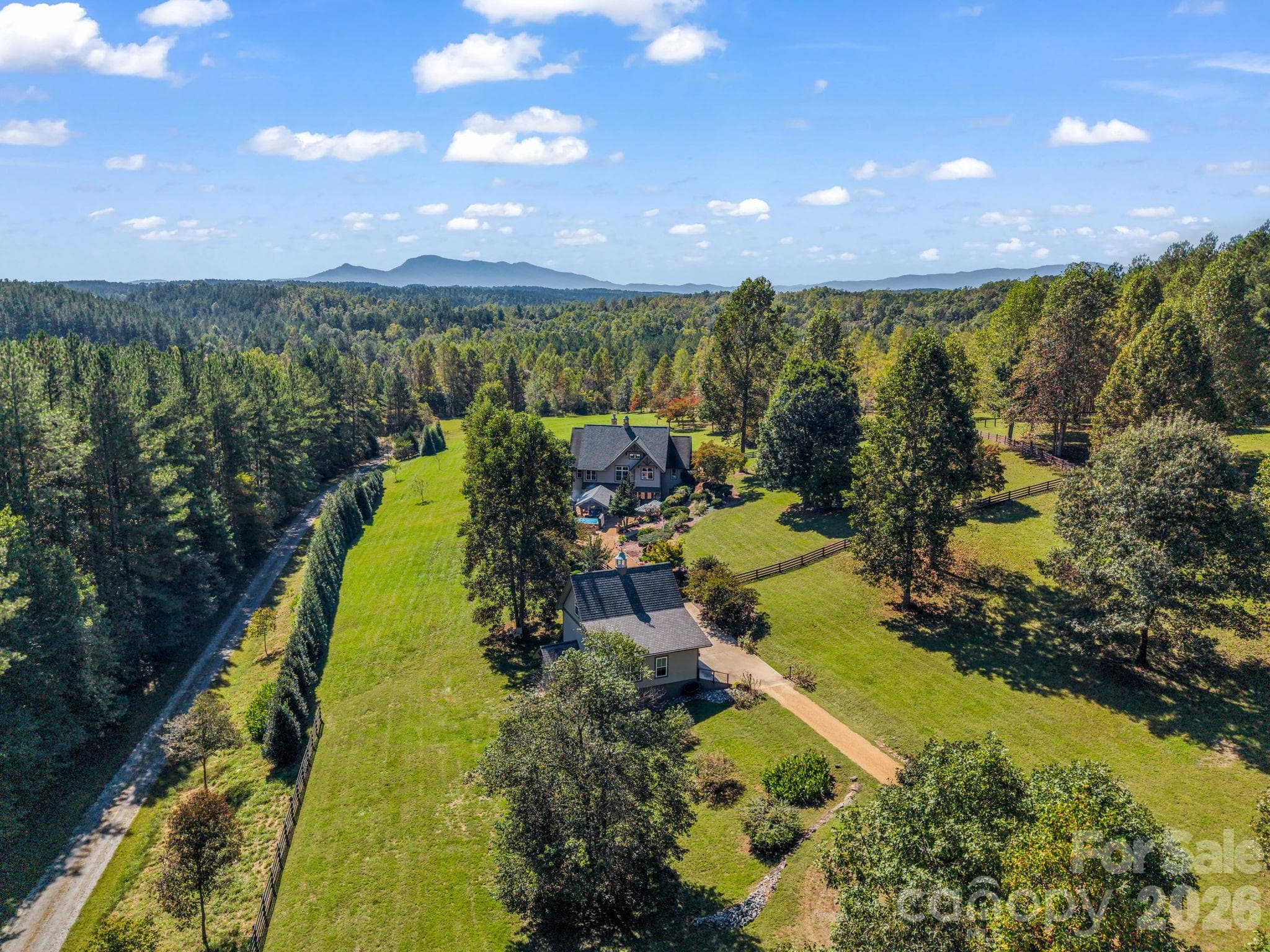 Aerial showcasing the pastures, long private drive, 3-car detached garage, pavilion with wood burning fireplace, swim spa and home - 140 Blazing Star Lane, Mill Spring