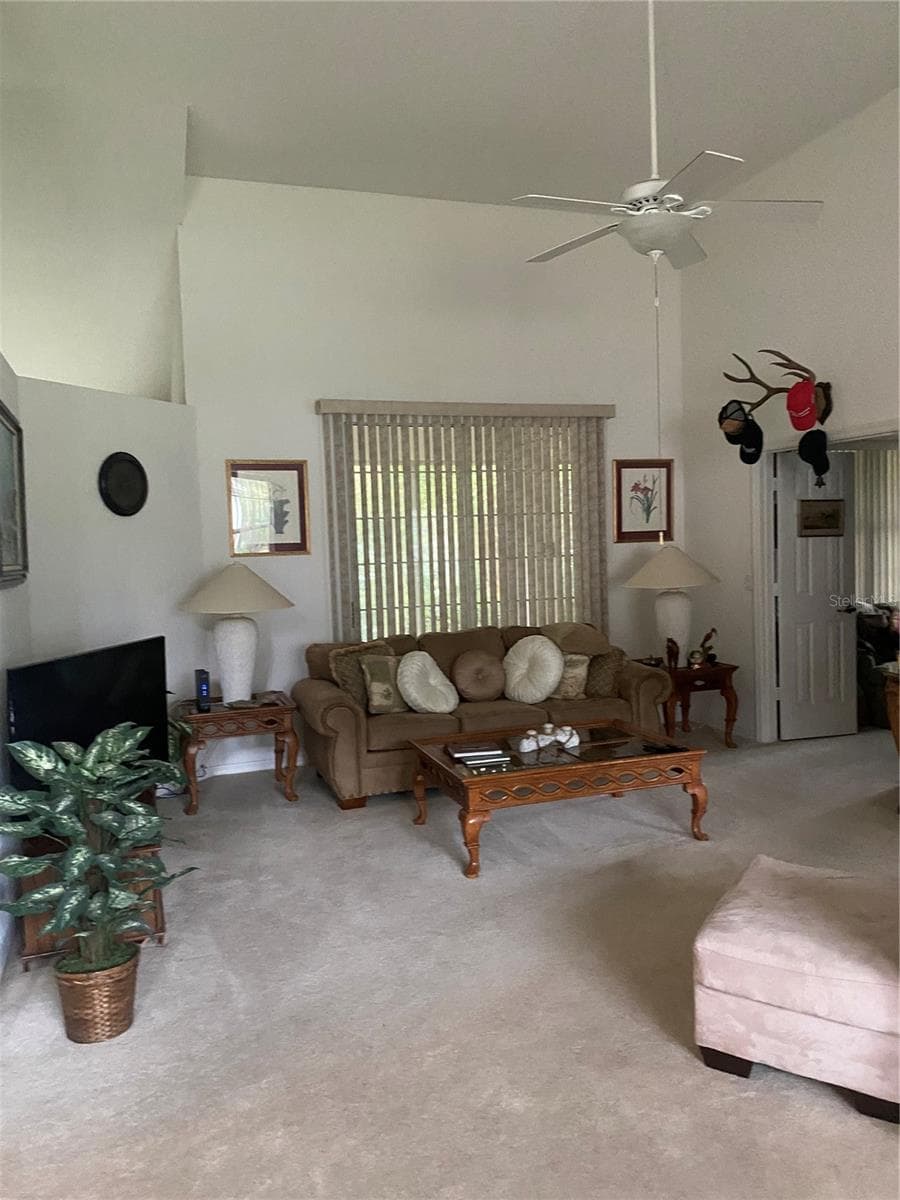 Living room area, clean carpet, high ceiling, ceiling fan with light, sliding glass door to the lanai area. - 11492 SW 82ND COURT RD, OCALA
