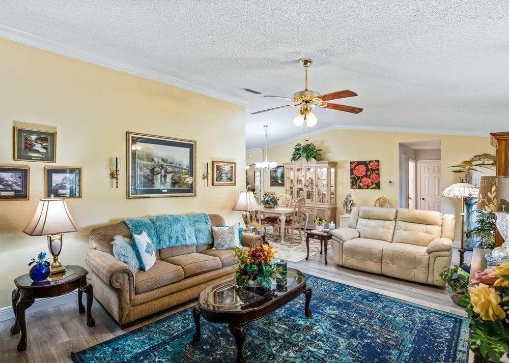 Inviting living area featuring wood-look vinyl flooring, crown molding, soft neutral walls, and a ceiling fan. The open layout connects seamlessly to the dining area, creating a comfortable space for everyday living and entertaining. - 17909 SE 99TH AVE, SUMMERFIELD