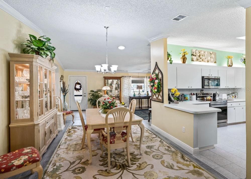 Inviting dining space with wood-look flooring, crown molding, and chandelier lighting opens to the living room and kitchen. - 17909 SE 99TH AVE, SUMMERFIELD