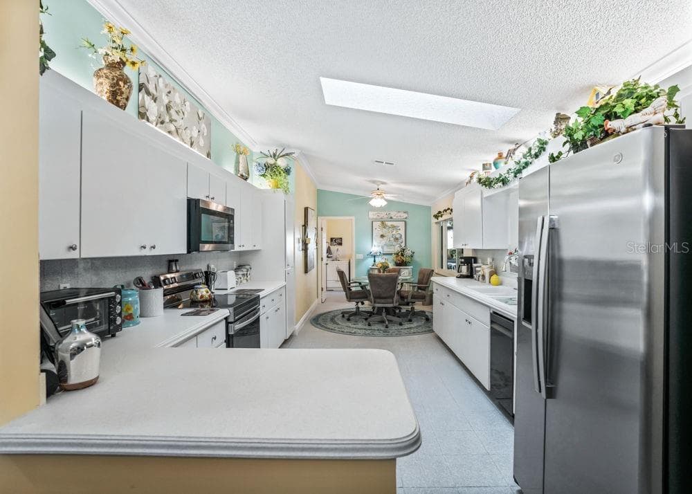 Bright kitchen featuring white cabinetry, stainless steel appliances, ample counter space, and a convenient breakfast bar. A skylight brings in natural light, while the adjoining breakfast nook offers a comfortable spot for casual dining. - 17909 SE 99TH AVE, SUMMERFIELD