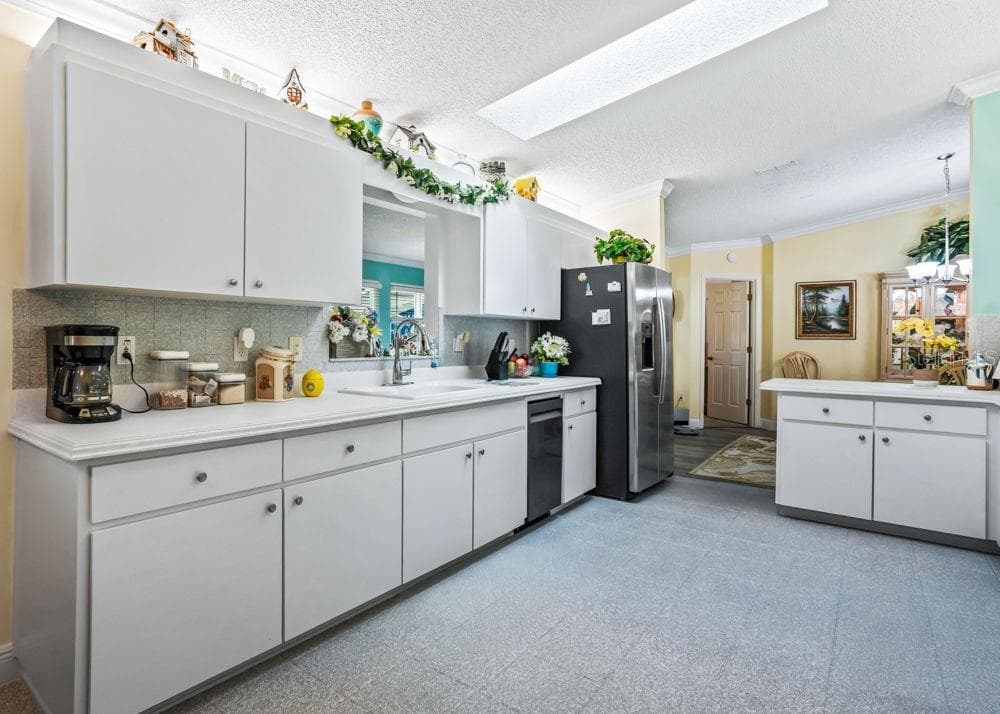 The bright kitchen features white cabinetry, generous counter space, a skylight, and refinished tile flooring. A convenient pass-through to the Florida room and an adjoining dining area create an inviting space for everyday living and entertaining. - 17909 SE 99TH AVE, SUMMERFIELD