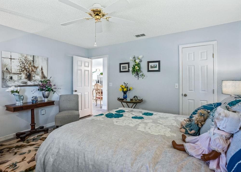 Another view of the second bedroom showcases soft blue walls, a ceiling fan, and wood-look flooring. The room offers space for additional seating, with a closet and convenient access to the hallway. - 17909 SE 99TH AVE, SUMMERFIELD