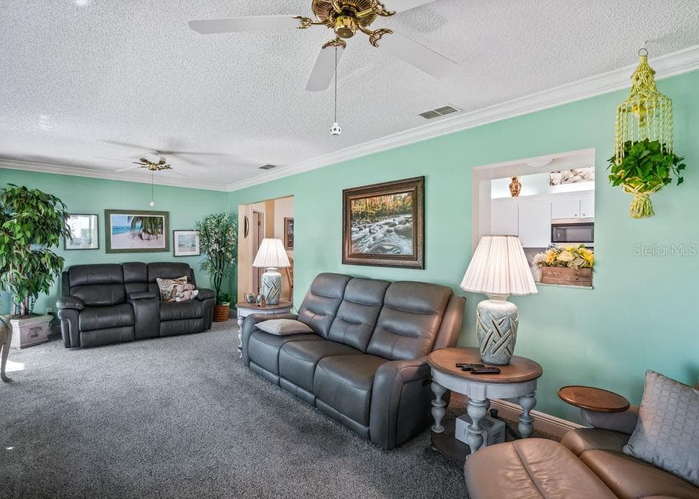 Another view of the spacious Florida room showcases soft aqua walls, crown molding, carpeting, and two ceiling fans. A convenient pass-through to the kitchen and ample seating space make this an inviting spot for relaxing or entertaining. - 17909 SE 99TH AVE, SUMMERFIELD