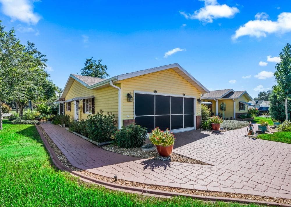 The screened two-car garage is complemented by a spacious brick-paver driveway and a matching walkway that leads around the house to the back patio. Beautiful landscaping, colorful flowers, and lush greenery create an inviting setting along the way. - 17909 SE 99TH AVE, SUMMERFIELD
