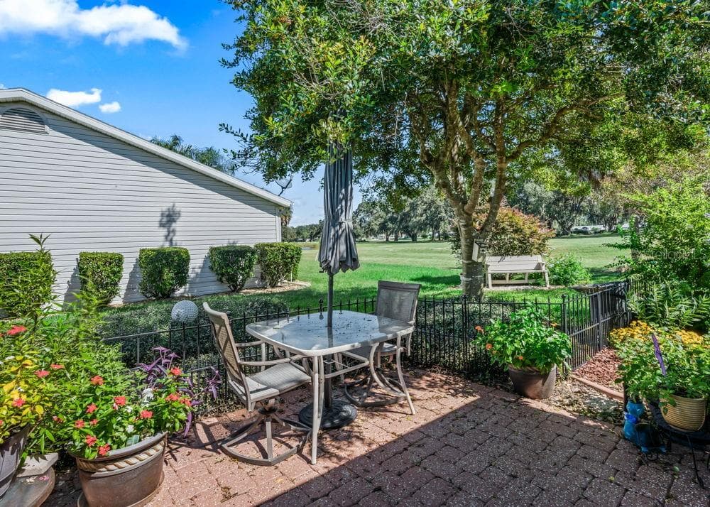 This charming brick-paver patio offers views of The Links golf course beneath the canopy of a mature shade tree. Colorful flowering plants, lush garden beds, and decorative black fencing create an inviting setting for outdoor dining or relaxing. - 17909 SE 99TH AVE, SUMMERFIELD