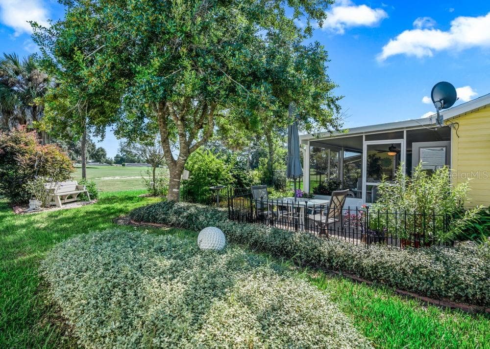 Beautifully landscaped backyard with a mature shade tree, lush groundcover, and colorful flowers that attract butterflies, all complemented by views of The Links golf course. A fenced brick-paver patio connects to the screened lanai, offering an inviting setting for outdoor dining and relaxation. - 17909 SE 99TH AVE, SUMMERFIELD
