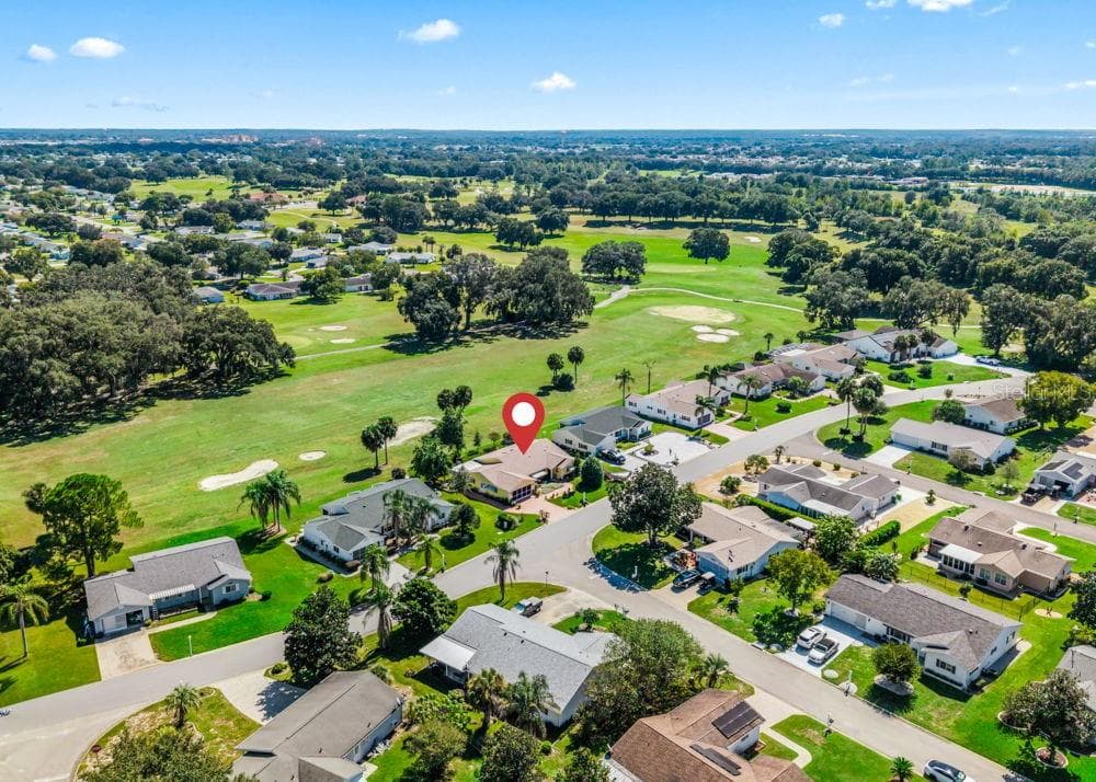 This aerial view showcases the home, marked by the red pin, directly along The Links golf course. Expansive fairways, sand bunkers, and mature trees provide a scenic backdrop, while the surrounding neighborhood features landscaped homes and winding streets. - 17909 SE 99TH AVE, SUMMERFIELD