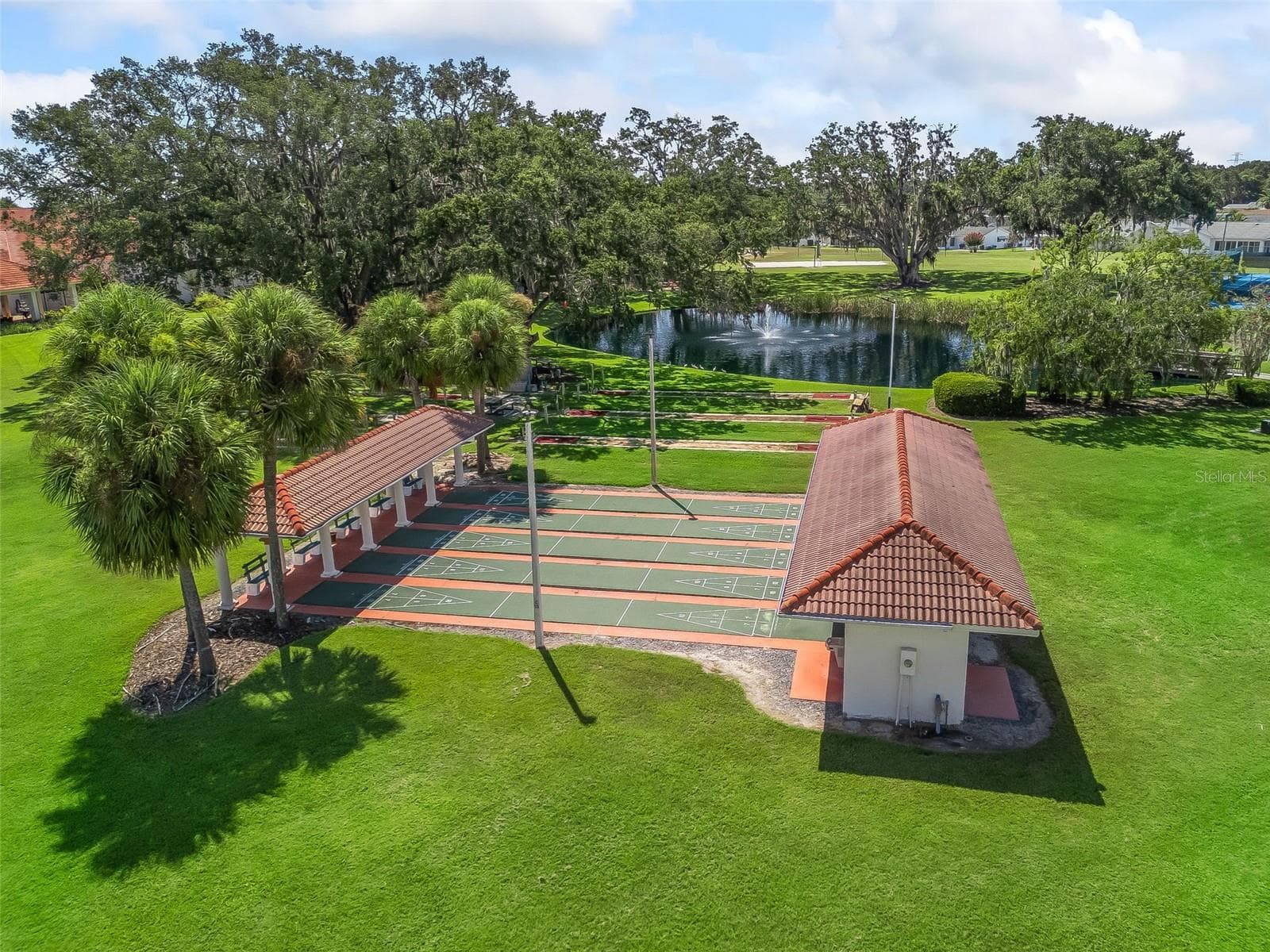 Spruce Creek South’s shuffleboard courts feature covered seating areas surrounded by palms and lush lawns. A scenic pond with a fountain and mature shade trees provides a peaceful backdrop for recreation and socializing. - 17909 SE 99TH AVE, SUMMERFIELD
