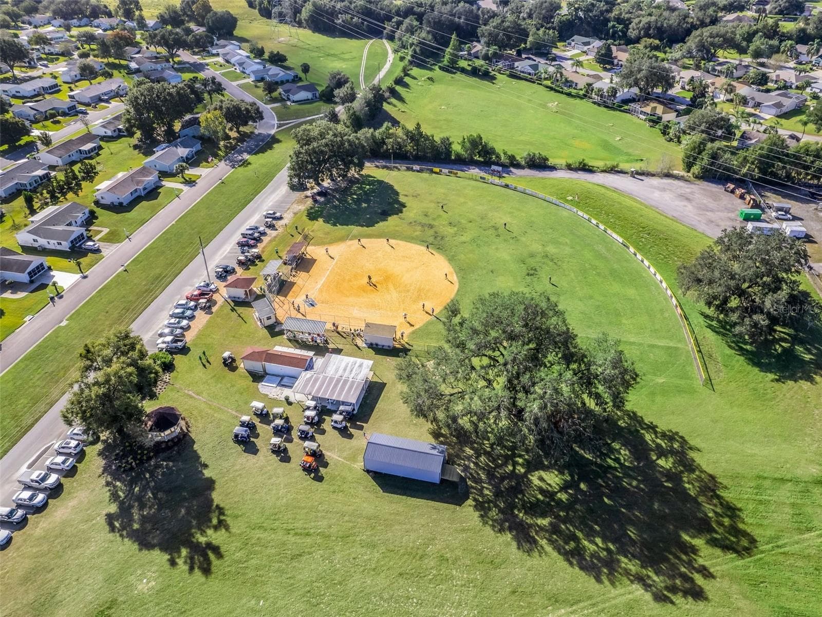 Spruce Creek South’s softball field features a spacious green outfield, covered seating, and mature shade trees. Players on the diamond and nearby golf cart parking capture the community’s active, welcoming atmosphere. - 17909 SE 99TH AVE, SUMMERFIELD