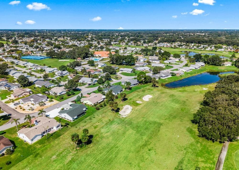 This aerial view showcases Spruce Creek South’s scenic golf course, sparkling ponds, and tree-lined residential streets. The clubhouse, pool, and tennis courts are visible nearby, highlighting the community’s inviting setting and variety of recreational amenities. - 17909 SE 99TH AVE, SUMMERFIELD
