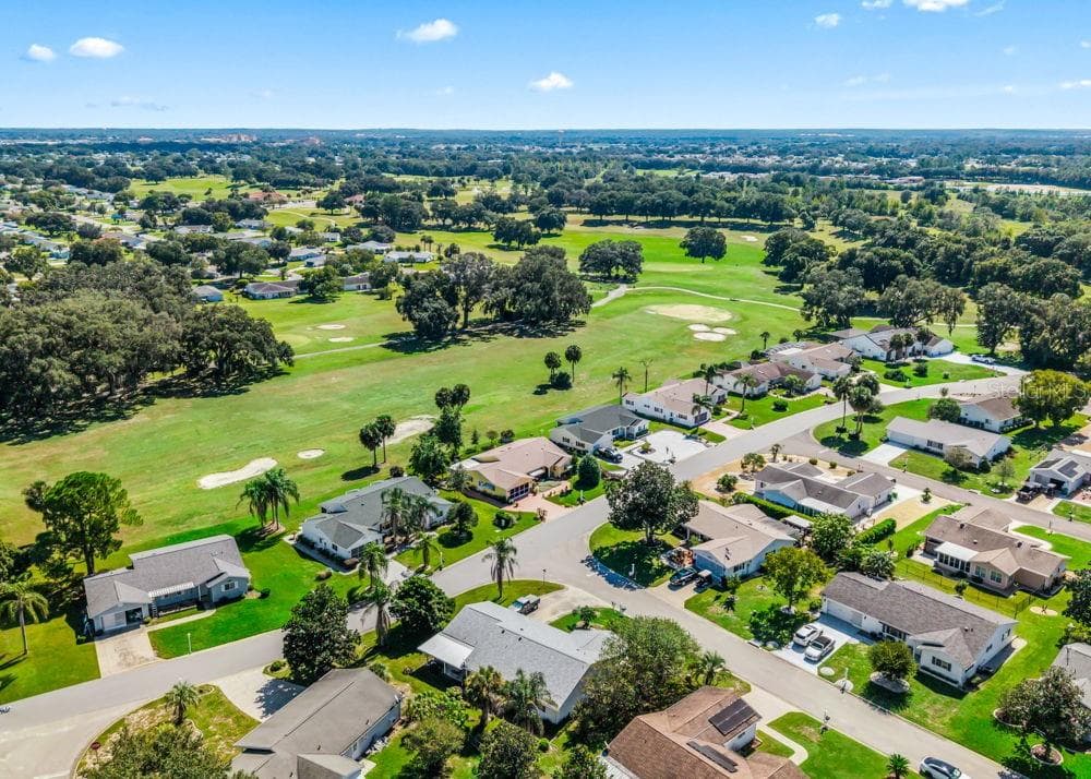 This aerial view highlights Spruce Creek South’s golf course setting, with sweeping fairways, sand bunkers, and mature oak trees. Homes along the course enjoy scenic surroundings, while landscaped yards and palm-lined streets add to the neighborhood’s Florida charm. - 17909 SE 99TH AVE, SUMMERFIELD