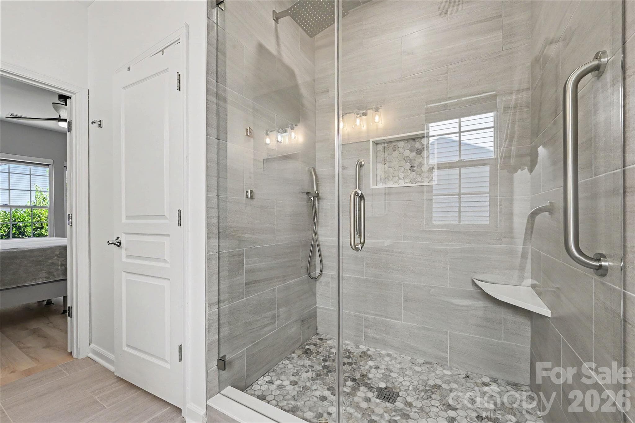Another view of the LUXURIOUS SHOWER in the Primary Bath showing custom ceiling to floor tile, tile floor pan, frameless glass door and surround, body jets, Rain shower, and grab handle. - 3054 Azalea Drive, Indian Land
