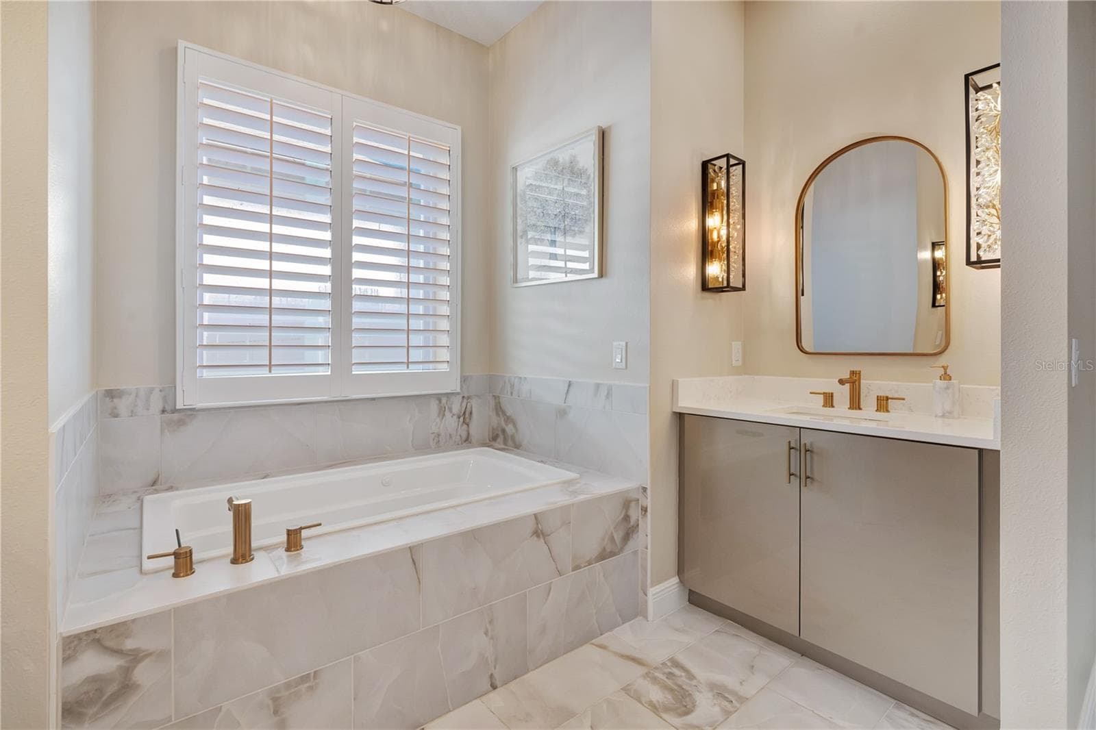 Relaxing bath retreat with a soaking tub beneath plantation shutters, decorative mirror and gold-tone fixtures. - 17600 LAKE STAR RD, WINTER GARDEN