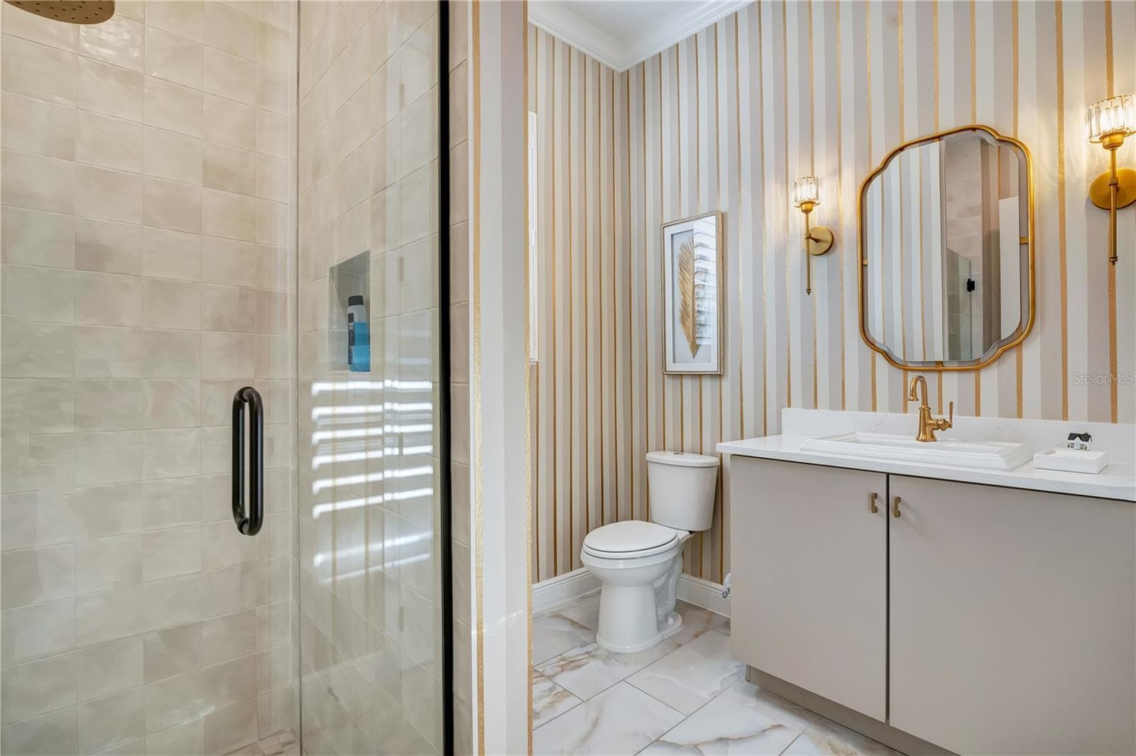 Designer bathroom with a glass-enclosed shower, striped accent wall and gold-tone fixtures. - 17600 LAKE STAR RD, WINTER GARDEN