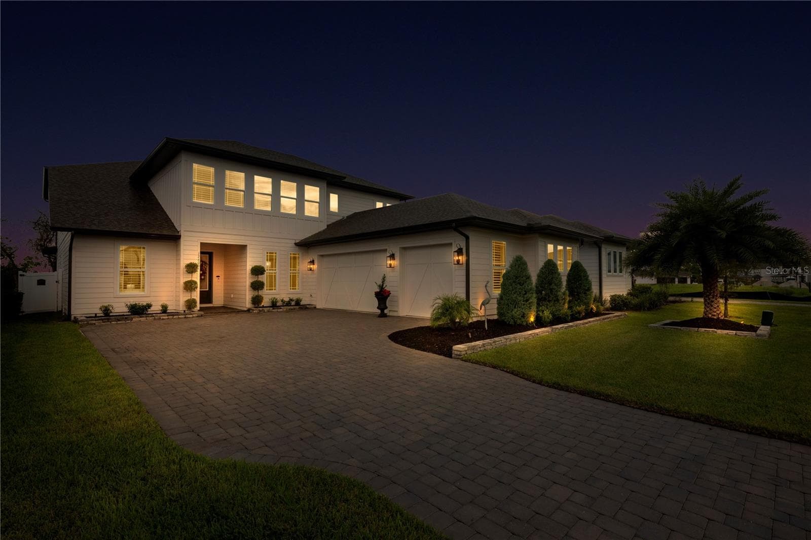 Evening exterior highlights illuminated garden beds and the landscaped front lawn. - 17600 LAKE STAR RD, WINTER GARDEN