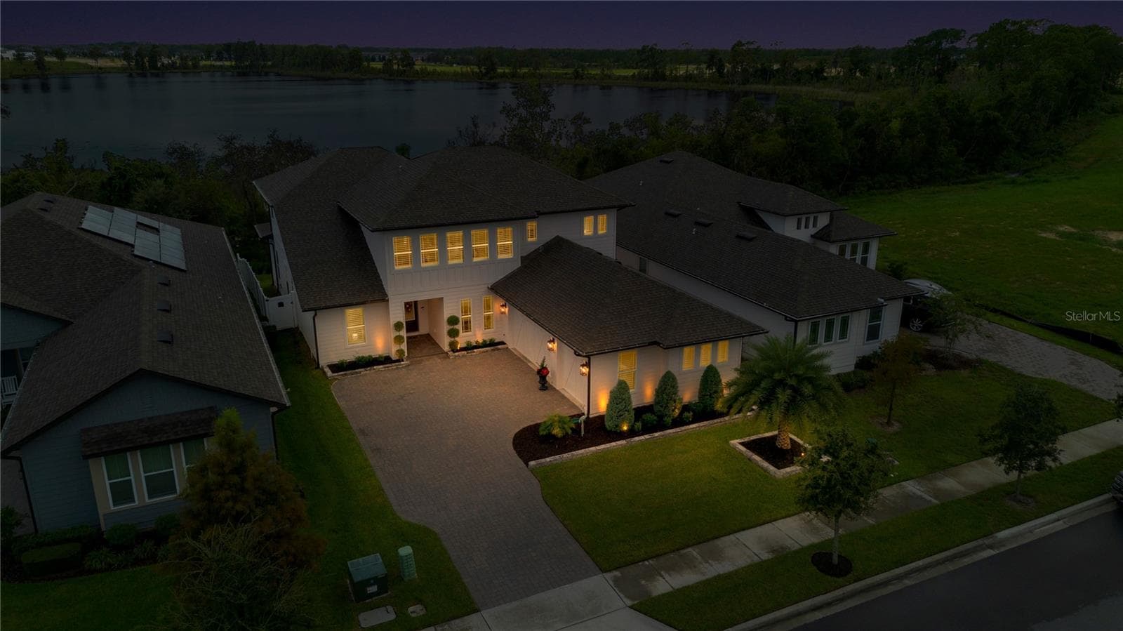 Twilight aerial showcases the home with the lake visible beyond the surrounding trees. - 17600 LAKE STAR RD, WINTER GARDEN