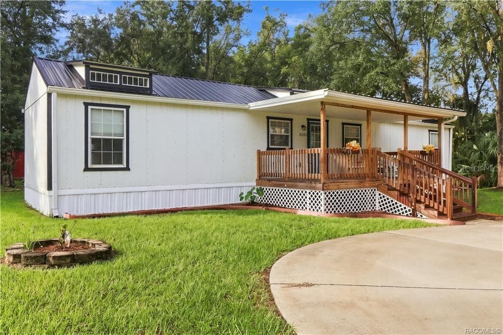 Front Exterior – Attractive white exterior w/contrasting dark trim, METAL ROOF & spacious covered wooden porch, surrounded by a lush green lawn. - 6230 W GLEN ROBBIN CT, CRYSTAL RIVER